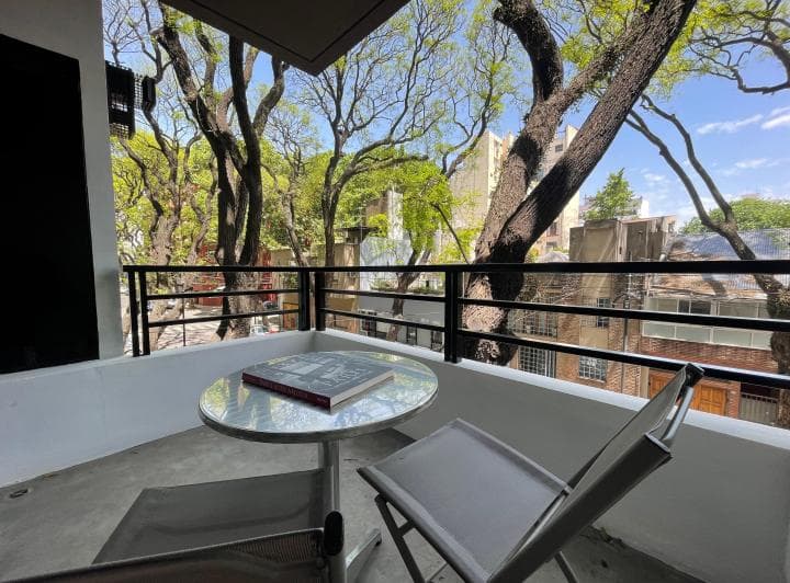 Balcón con mesa y silla, con vista a los árboles de la calle