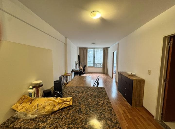 Living-comedor con mesa, sillas, escritorio y ventana al fondo, piso de madera.