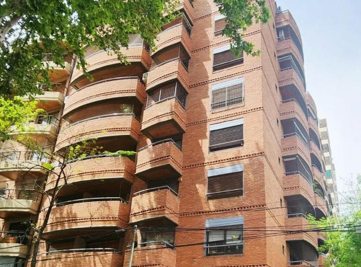 Edificio de ladrillo con múltiples balcones curvos y persianas en las ventanas.