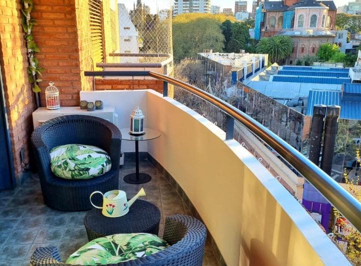 Balcón con sillas de ratán, mesita auxiliar y vista panorámica a la ciudad.