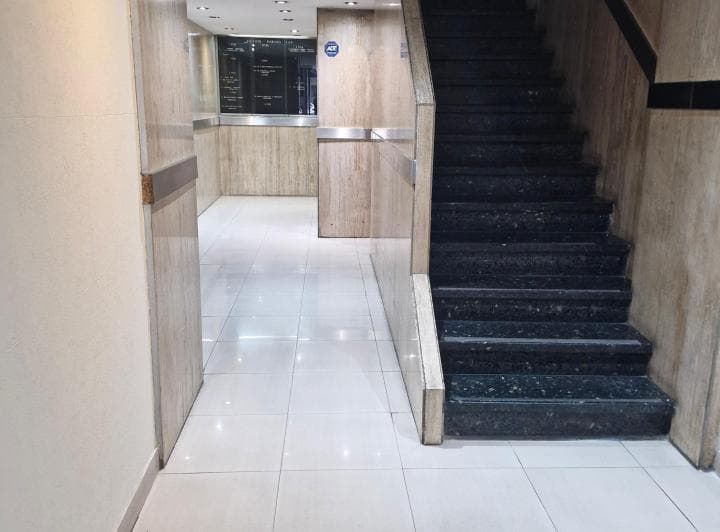 Hall de entrada del edificio con escalera de granito y pisos claros.
