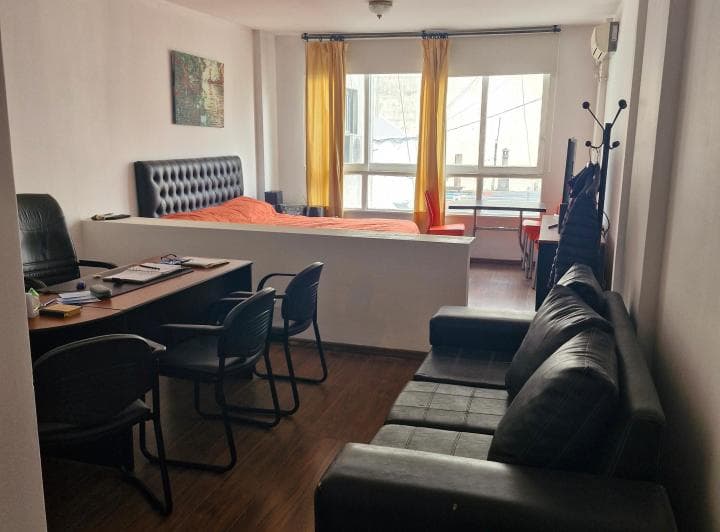 Ambiente principal con sofá, escritorio, cama al fondo y ventanal.