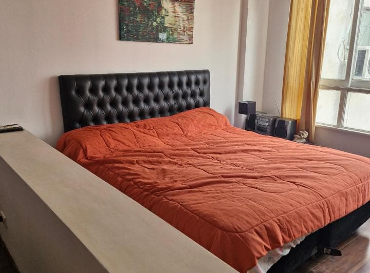 Dormitorio con cama doble de sábanas naranjas y cabecero tapizado.