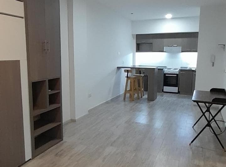 Living con cocina integrada, barra con banquetas, estantes y escritorio plegable.