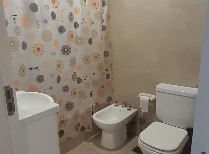 Baño completo con inodoro, bidet, lavatorio y cortina de ducha estampada.