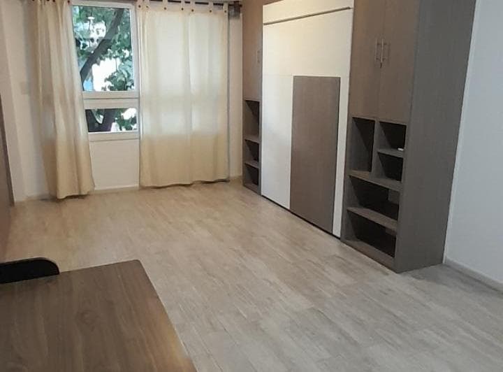 Dormitorio con cama rebatible, estantes integrados y ventana con cortinas.