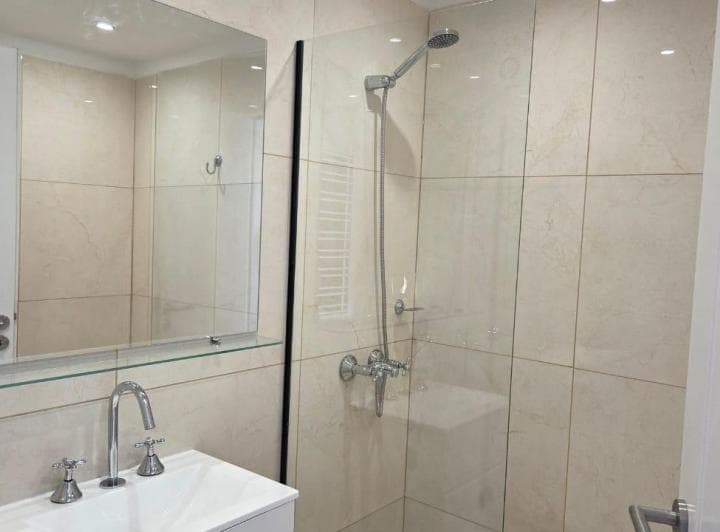 Baño con ducha, mampara de vidrio, vanitory y espejo.