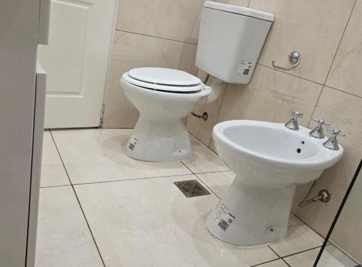 Baño con inodoro, bidet y azulejos claros en las paredes.