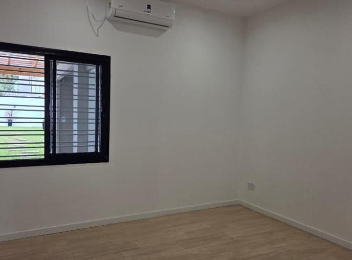 Dormitorio vacío con ventana grande, piso de madera y aire acondicionado.