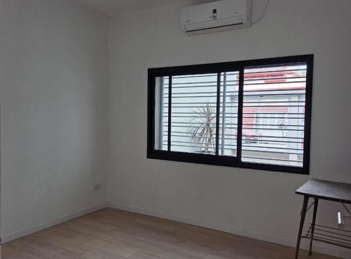 Dormitorio vacío con ventana grande, piso de madera y aire acondicionado.