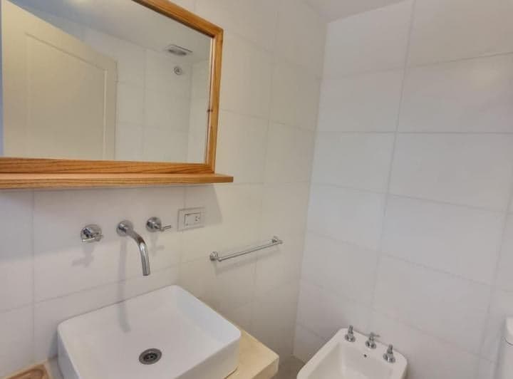 Baño con bidet, lavatorio blanco y espejo con marco de madera.