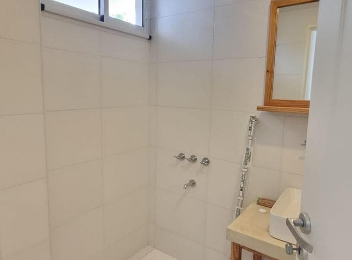 Baño con ducha, lavatorio y espejo, azulejos blancos.