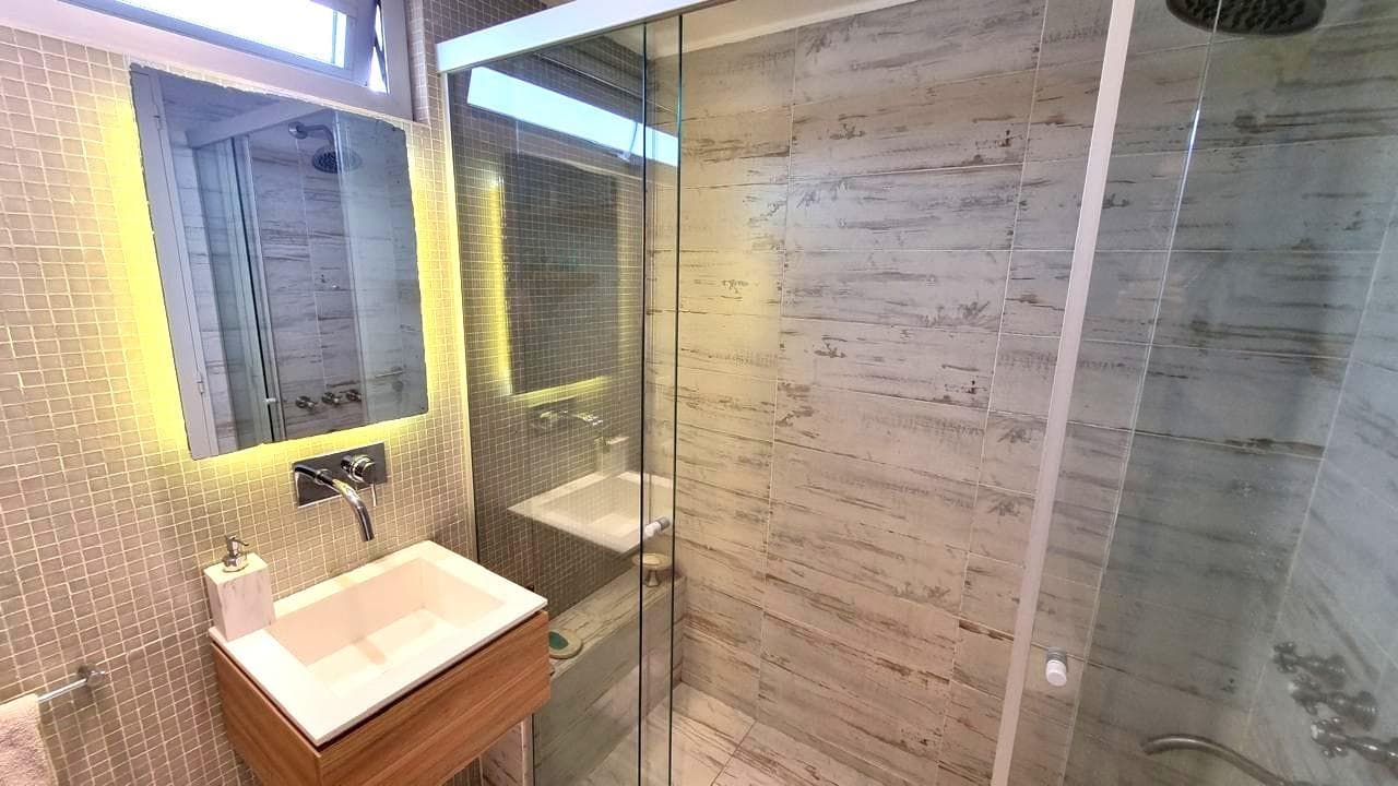 Baño completo con ducha con mampara de vidrio y vanitory con espejo iluminado.
