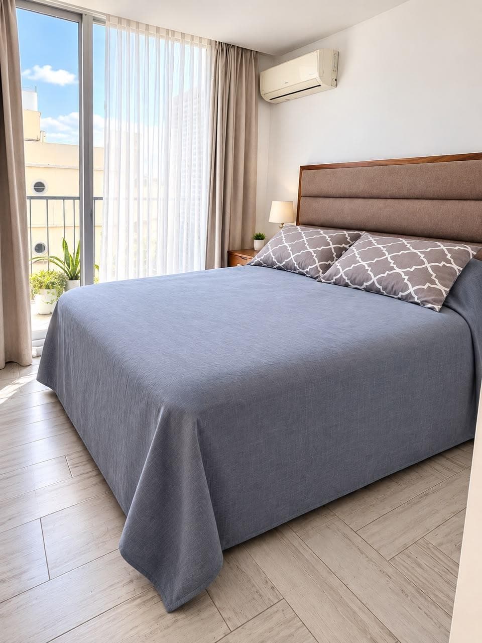 Dormitorio principal con cama doble, respaldo de madera, ventanal y aire acondicionado.
