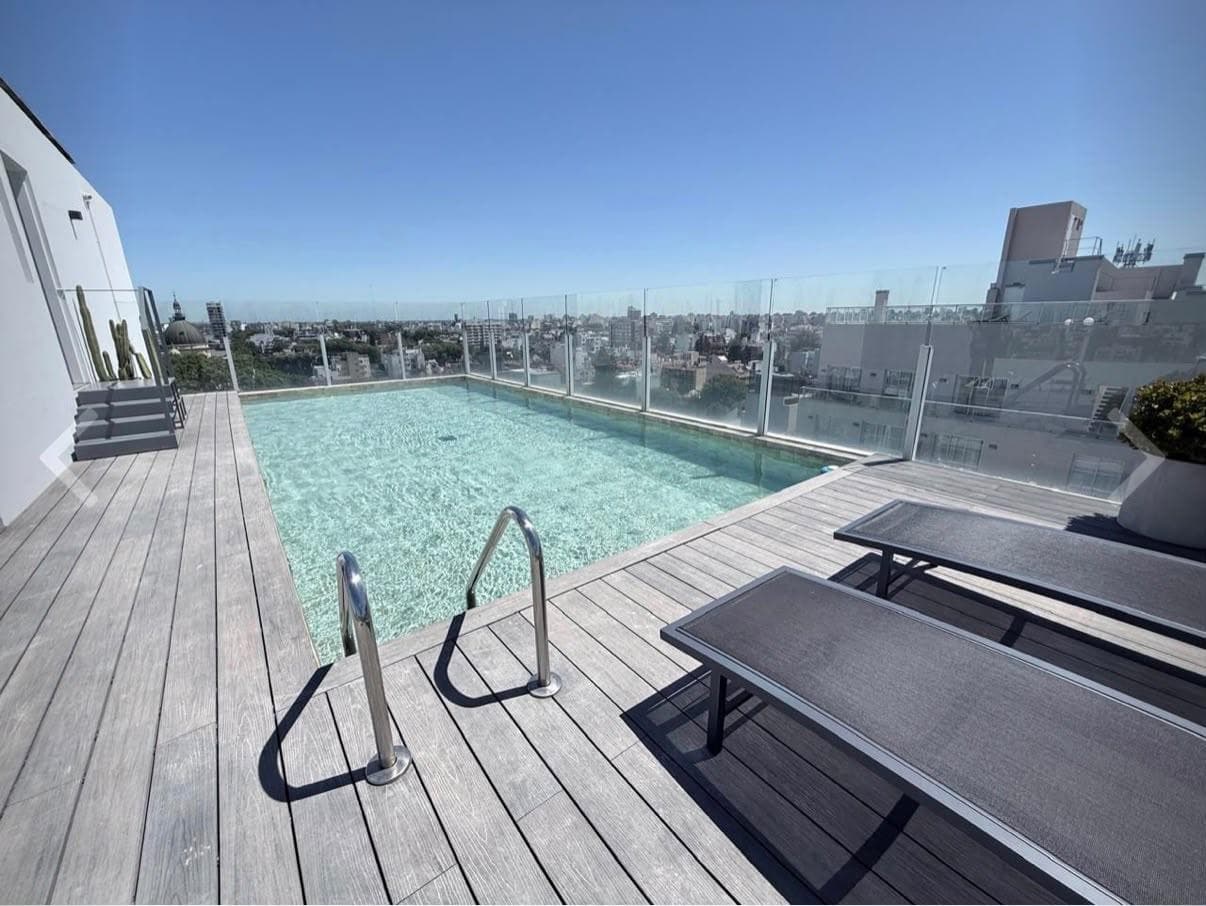 Pileta rectangular en terraza con reposeras y vista panorámica de la ciudad.