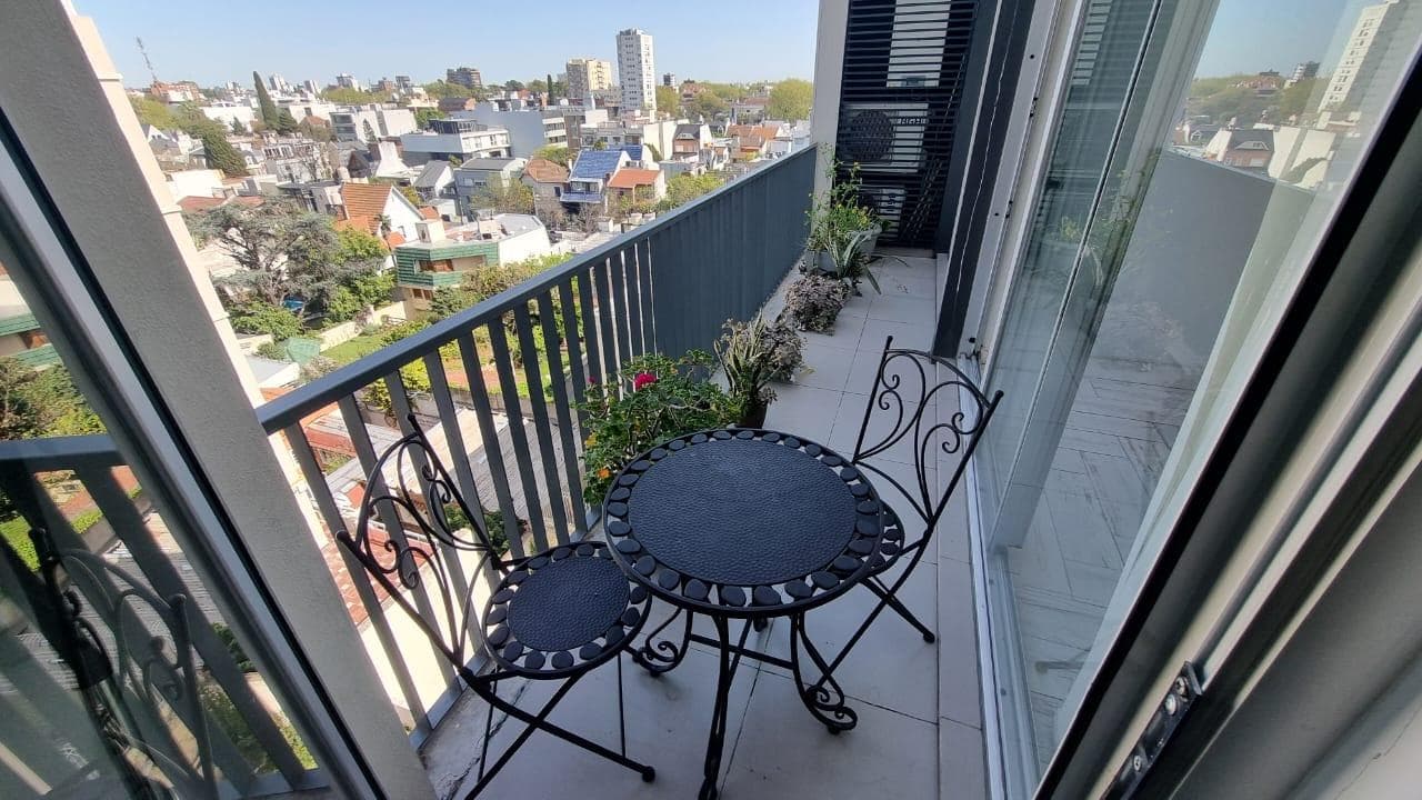 Balcón terraza con juego de mesa y sillas de hierro y vista a la ciudad.