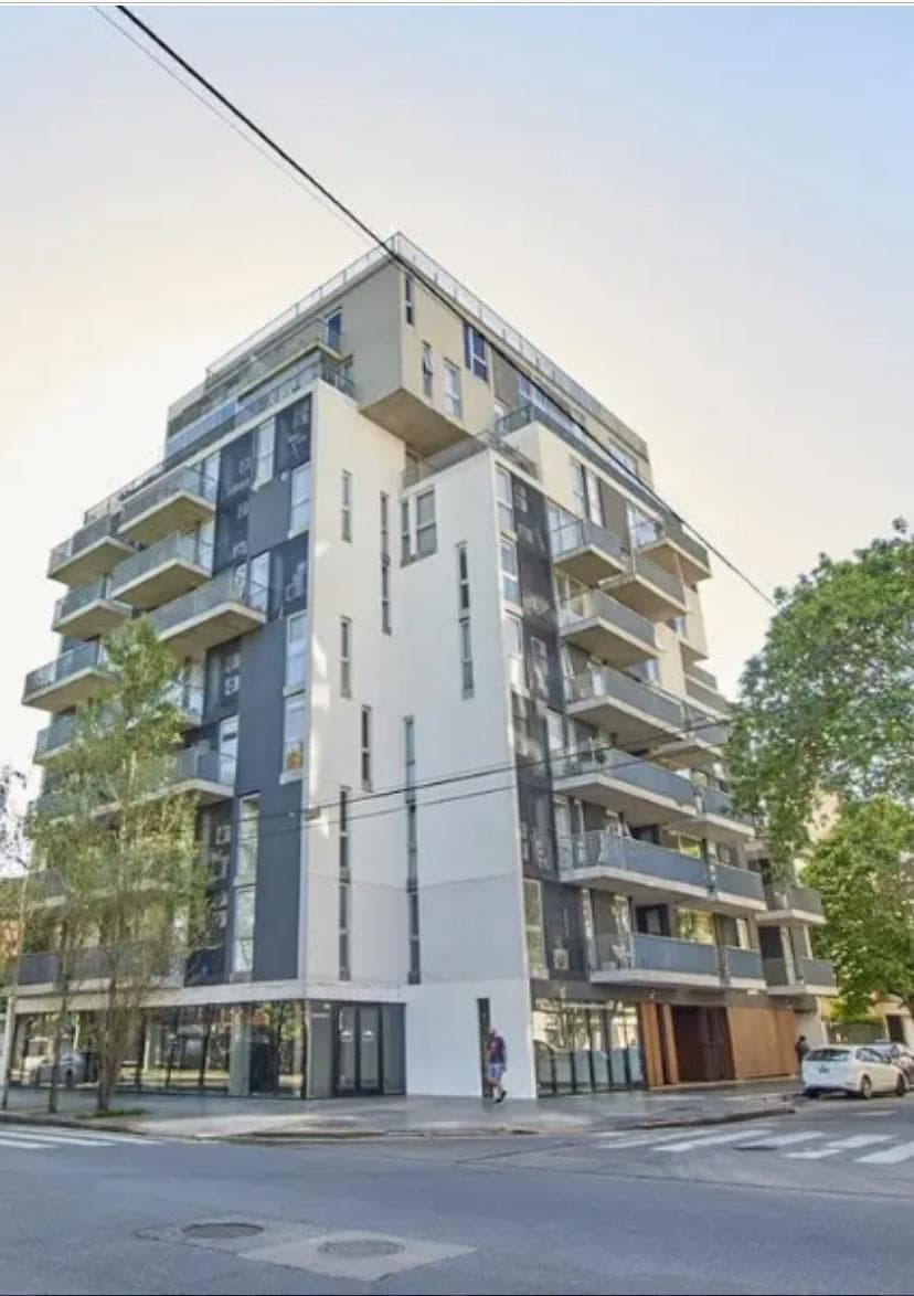 Edificio moderno con balcones, fachada en tonos grises y blancos en esquina.