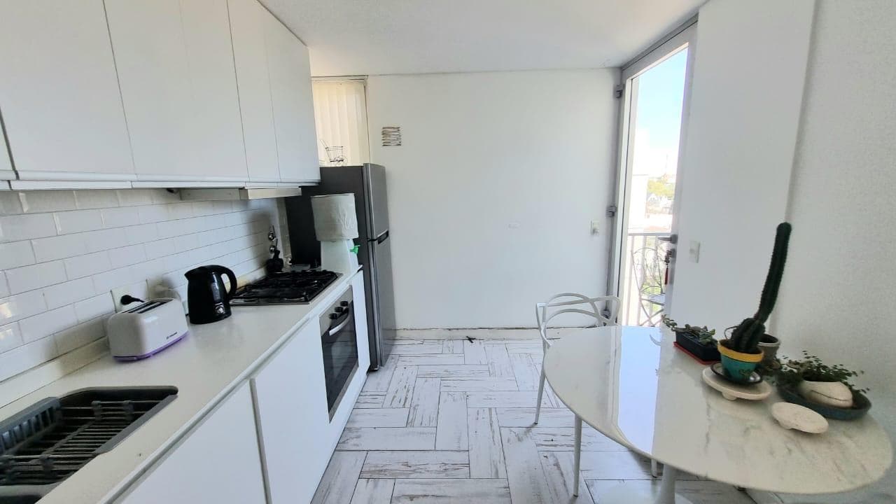 Cocina con mesada, anafe, horno, heladera, mesa redonda y puerta balcón.