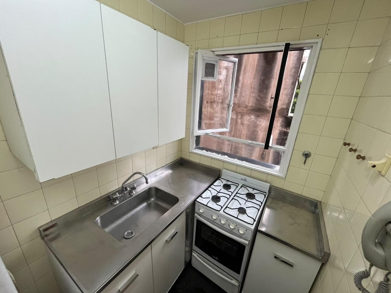 Cocina con mesada de acero inoxidable, bacha, anafe, horno y alacenas.