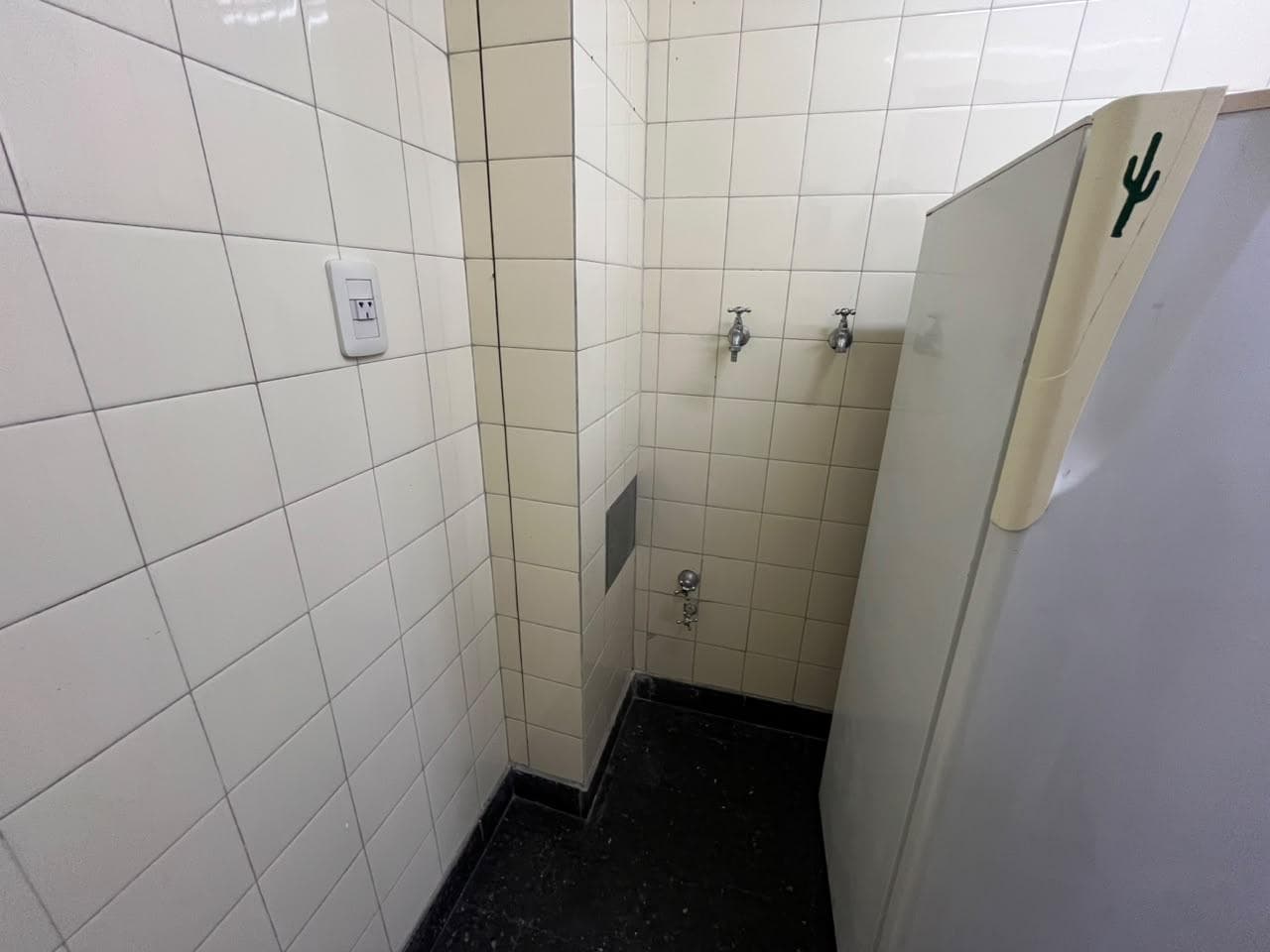 Lavadero con piso de baldosas negras, azulejos blancos y grifería.