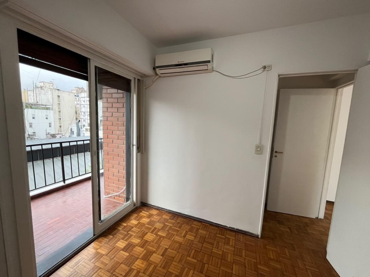 Dormitorio con piso de parquet, ventana, aire acondicionado y puerta.