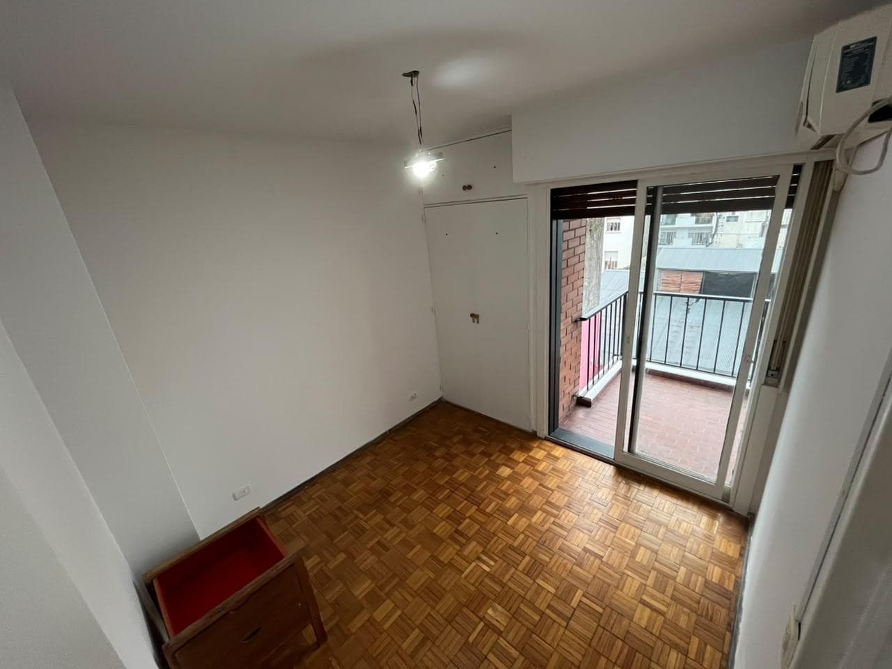 Dormitorio con piso de parquet, ventana al balcón y aire acondicionado.
