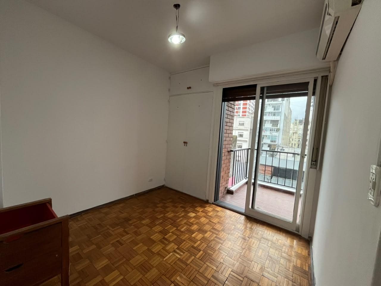 Dormitorio con piso de parquet, placard y ventana al balcón.