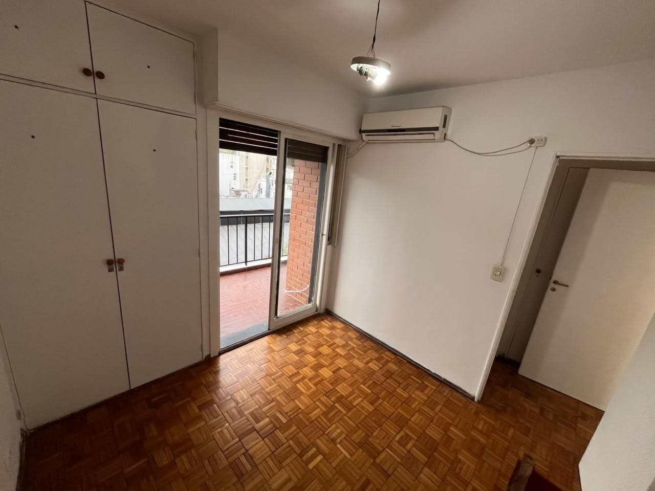 Dormitorio con placard empotrado, piso de parquet y ventana al balcón.