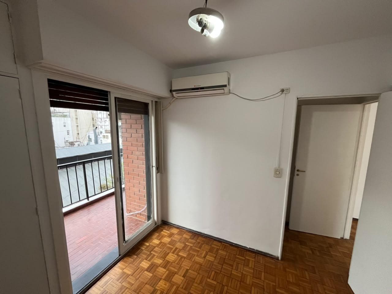 Dormitorio con piso de parquet, ventana con persiana y aire acondicionado.