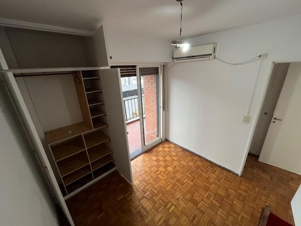 Dormitorio con placard abierto, piso de parquet y ventana.