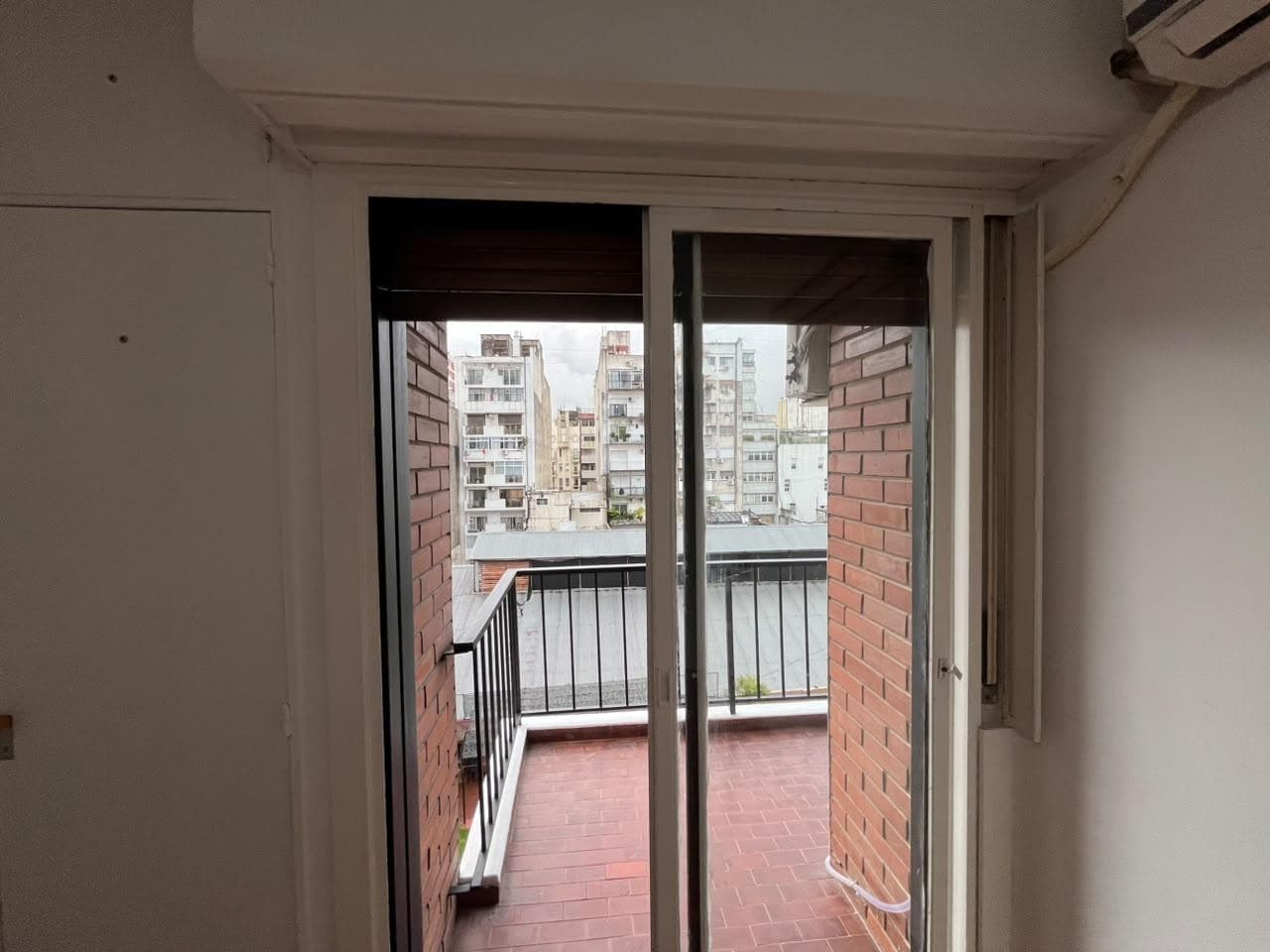 Balcón con rejas, piso de ladrillo a la vista y vista a edificios.
