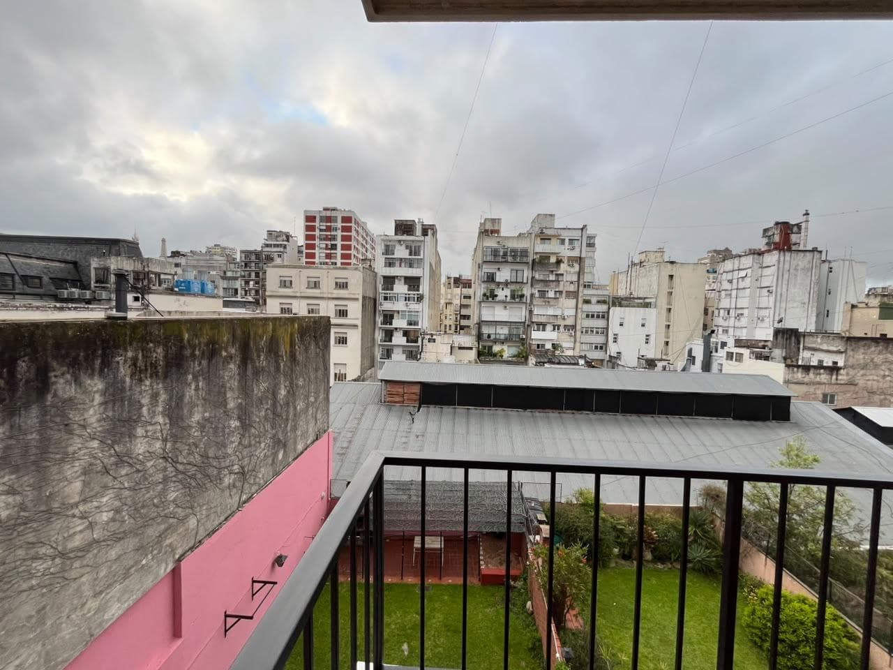 Vista desde balcón a patio verde, edificios y cielo nublado.
