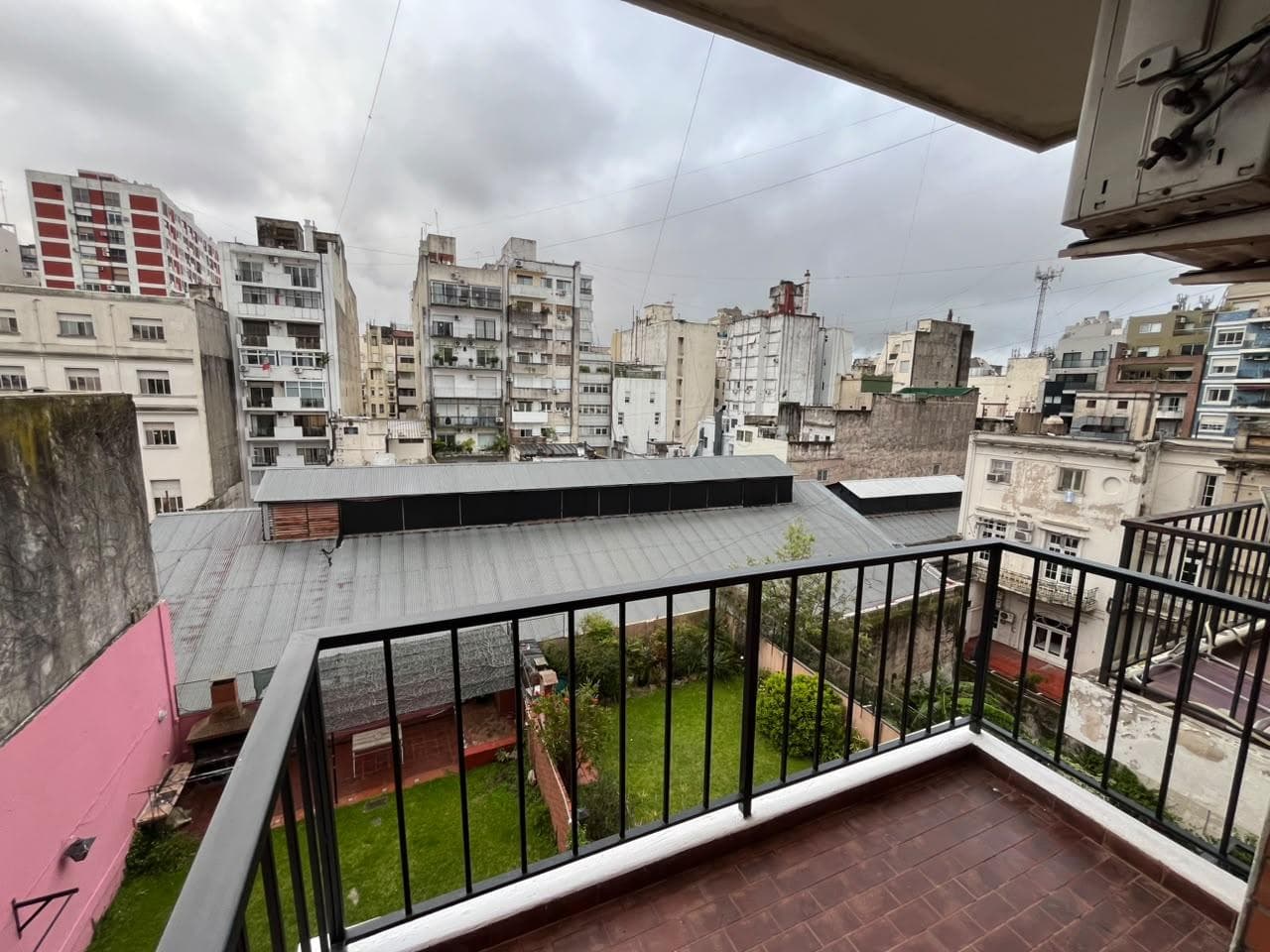 Vista desde balcón a patio verde y edificios de la ciudad.