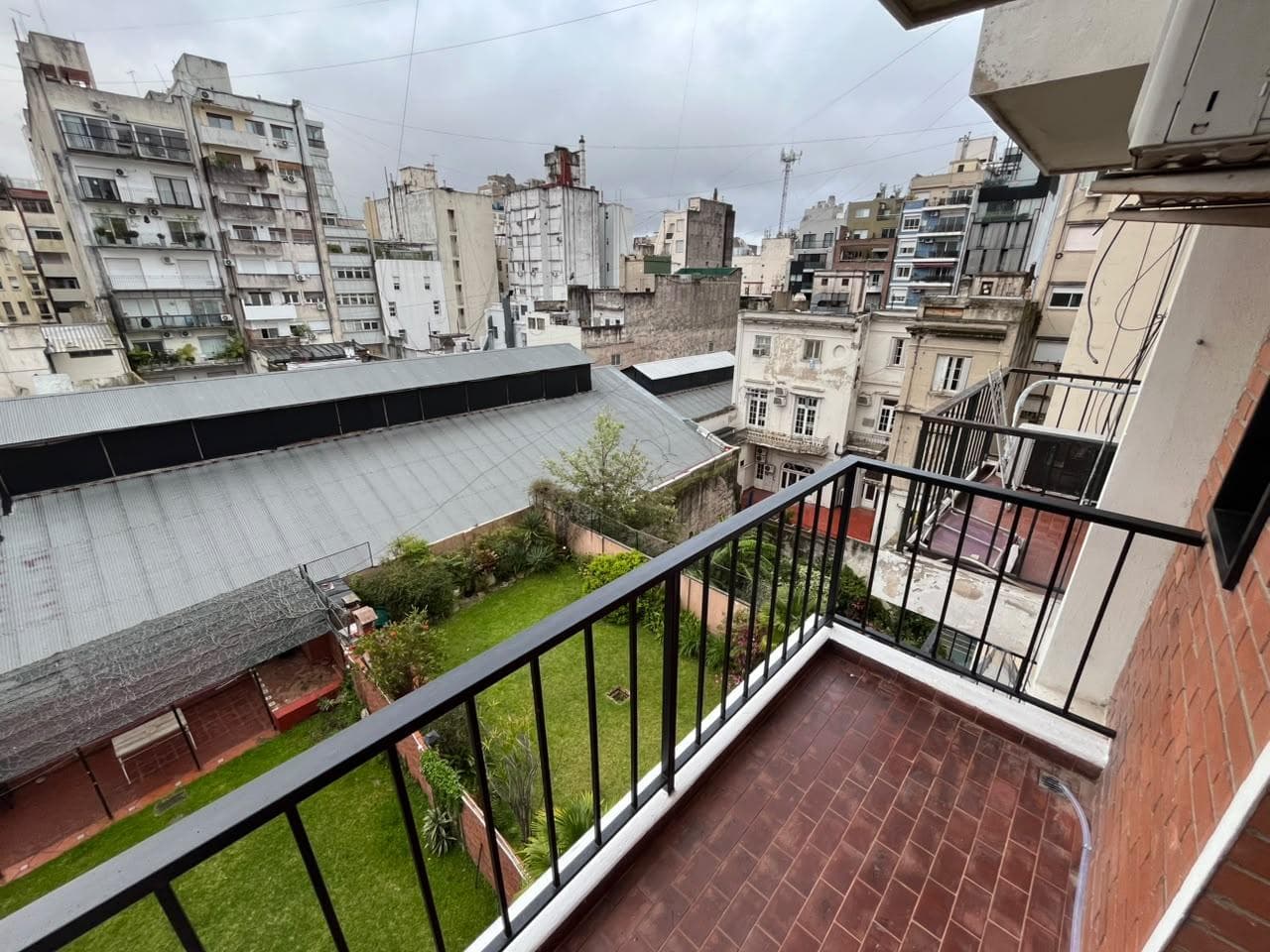 Vista desde balcón a patio verde y edificios de la ciudad.