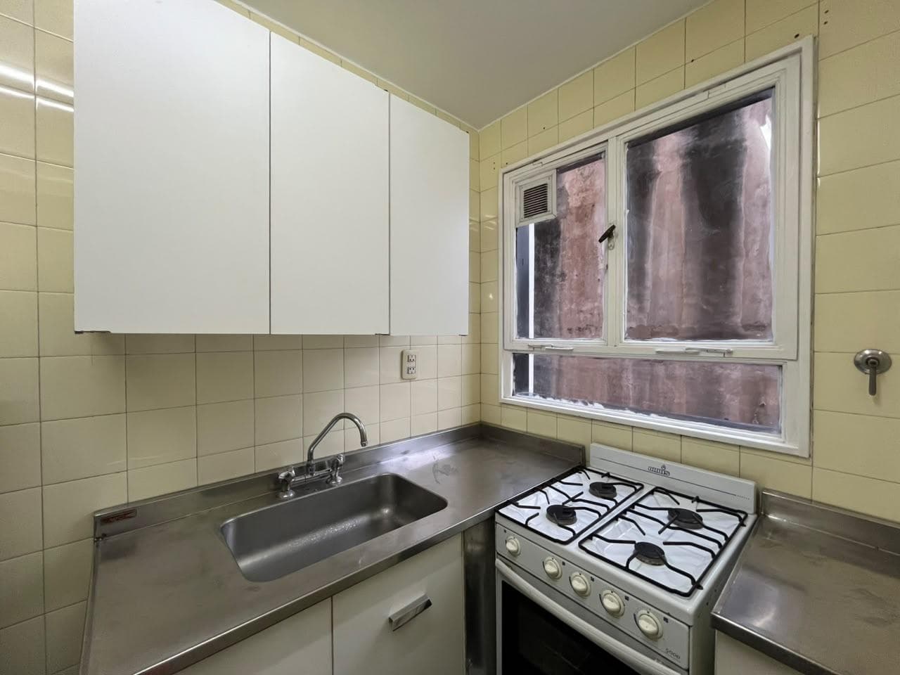 Cocina con mesada de acero, bacha, anafe, horno y alacenas.