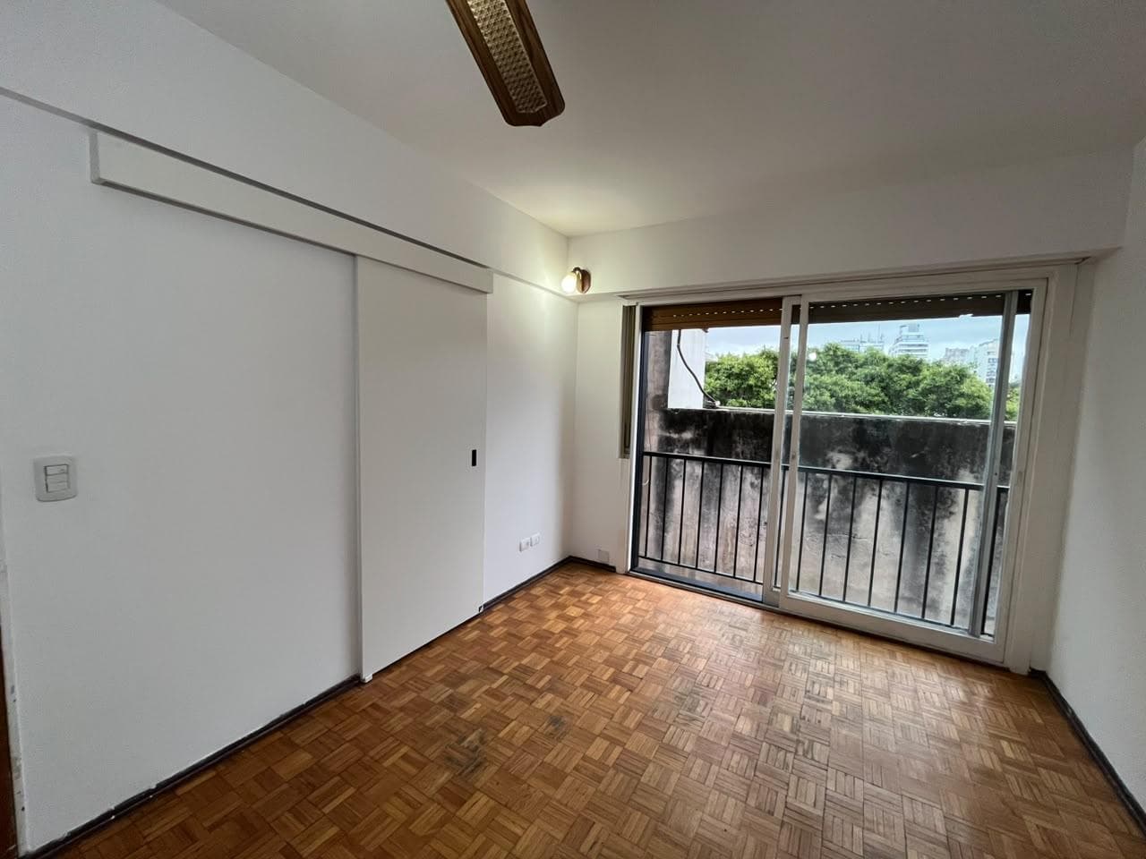 Dormitorio con piso de parquet, placard y ventana al balcón.