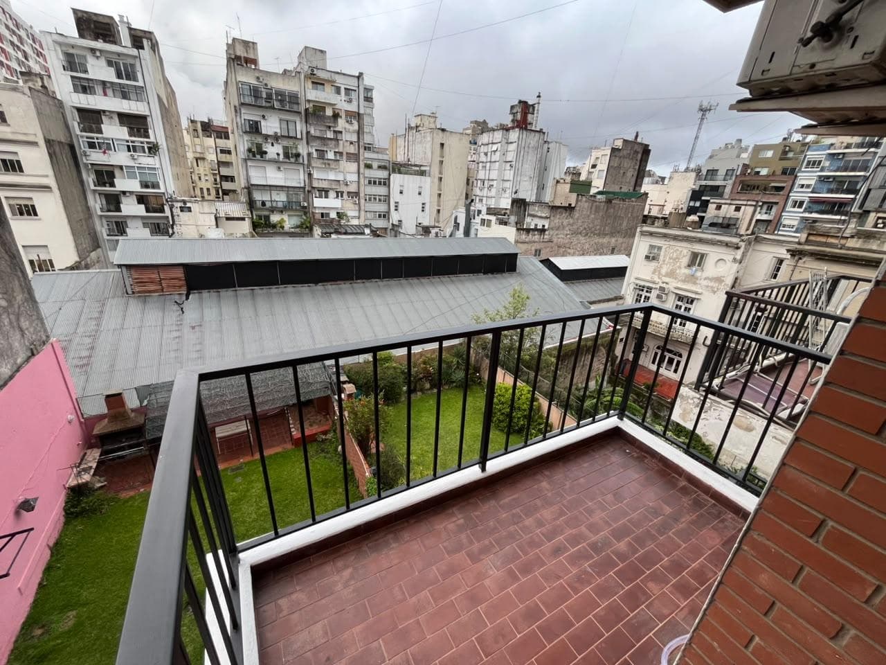 Balcón con rejas y vista a edificios de la ciudad y patio.