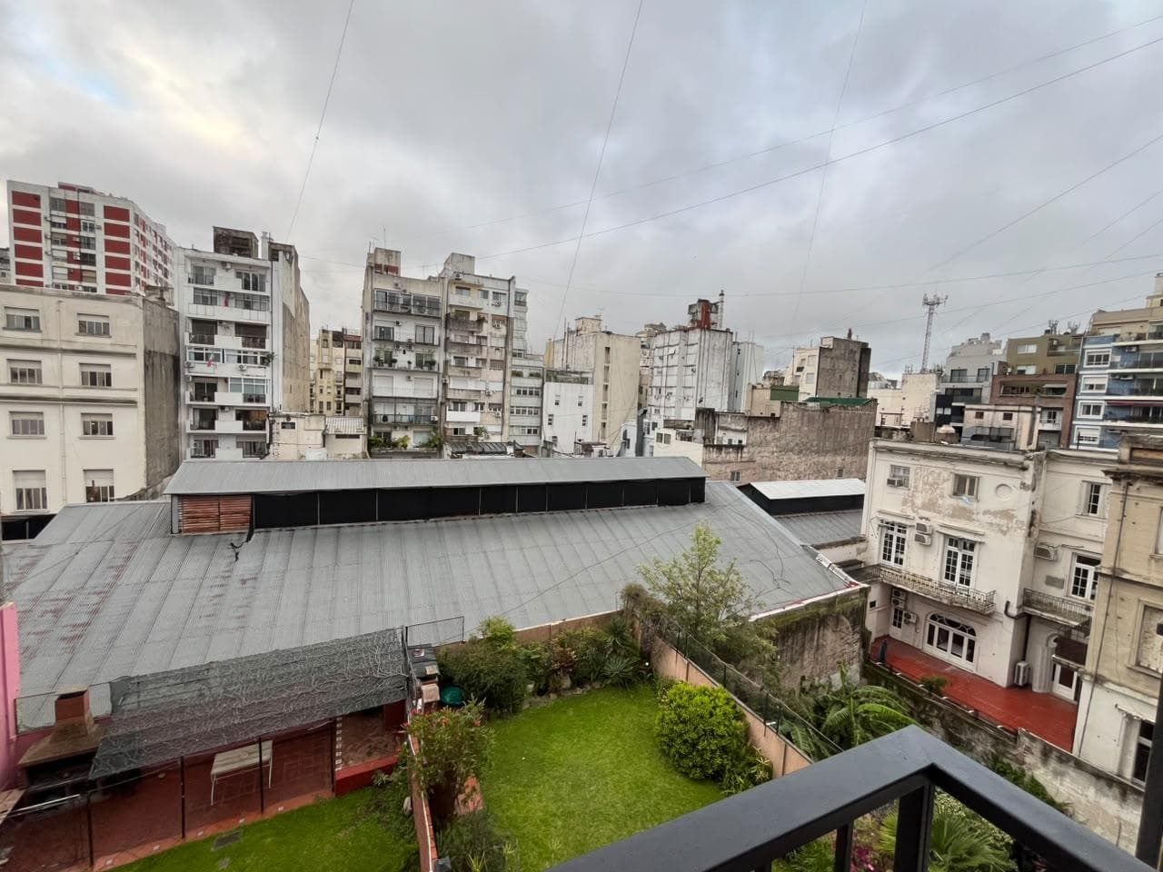 Vista desde balcón a patio verde, edificios y cielo nublado.