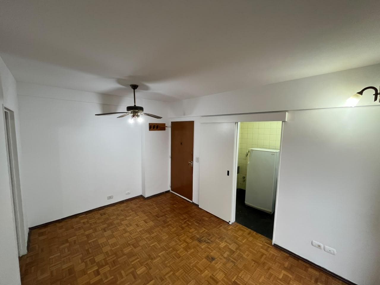 Living vacío con piso de parquet, puerta principal y puerta a cocina.