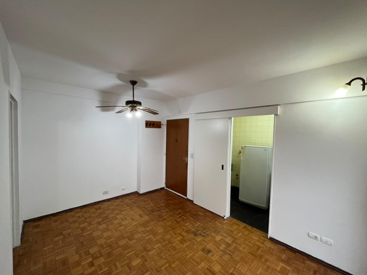 Living vacío con piso de parquet, puerta principal y puerta a cocina.