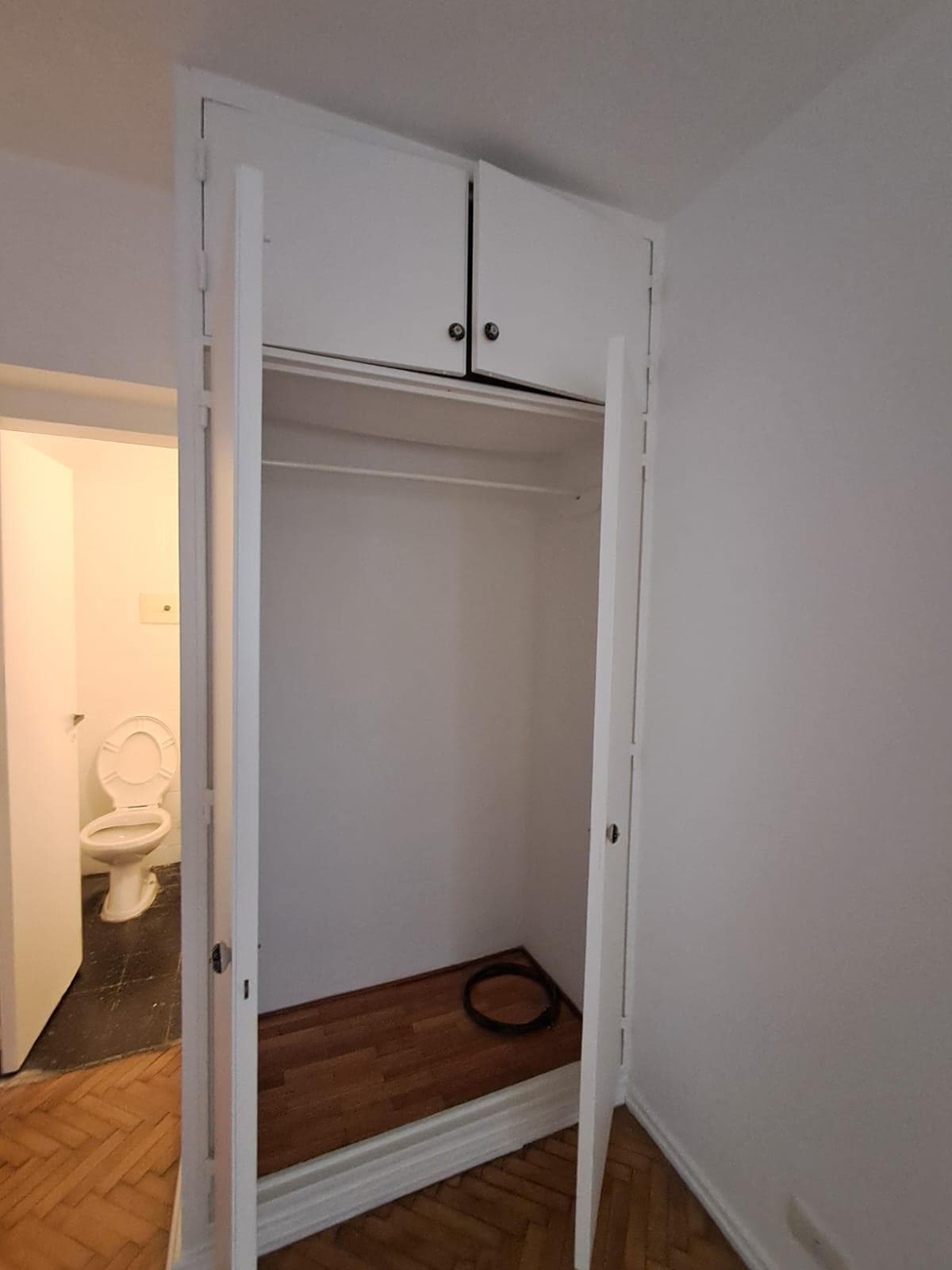 Placard abierto con barra para colgar ropa, al lado del baño.