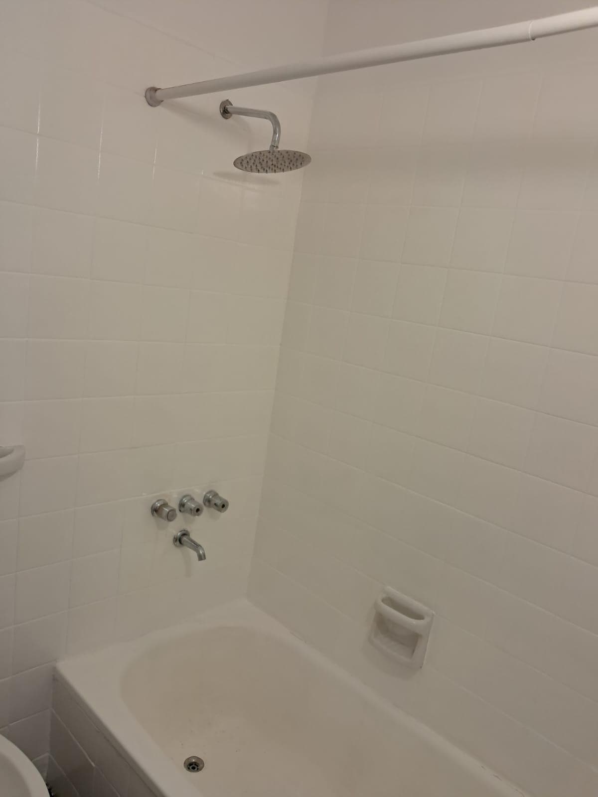 Ducha con flor de lluvia y grifería de tres llaves en bañera.