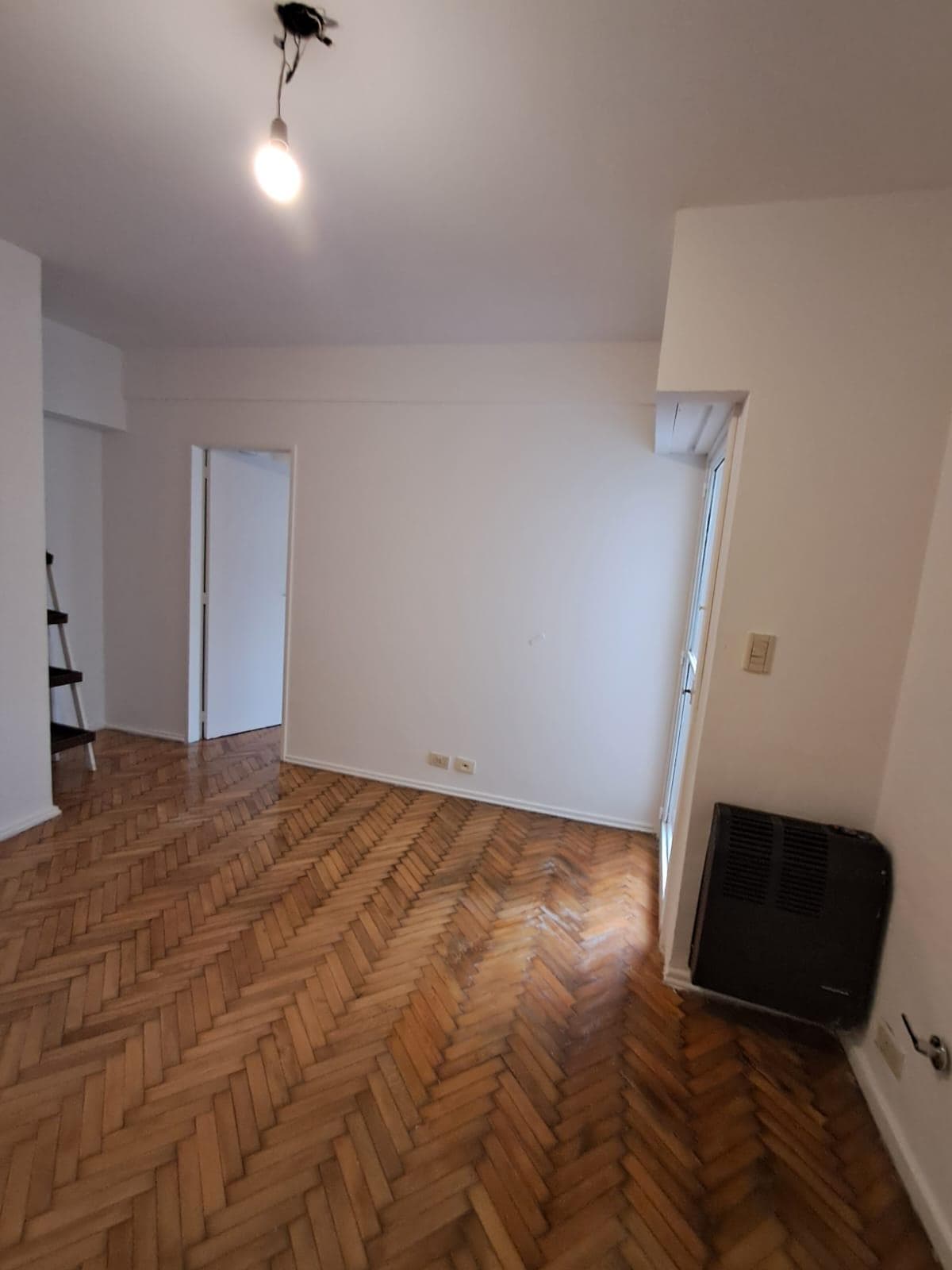 Amplio living vacío con piso de madera y ventana al balcón.