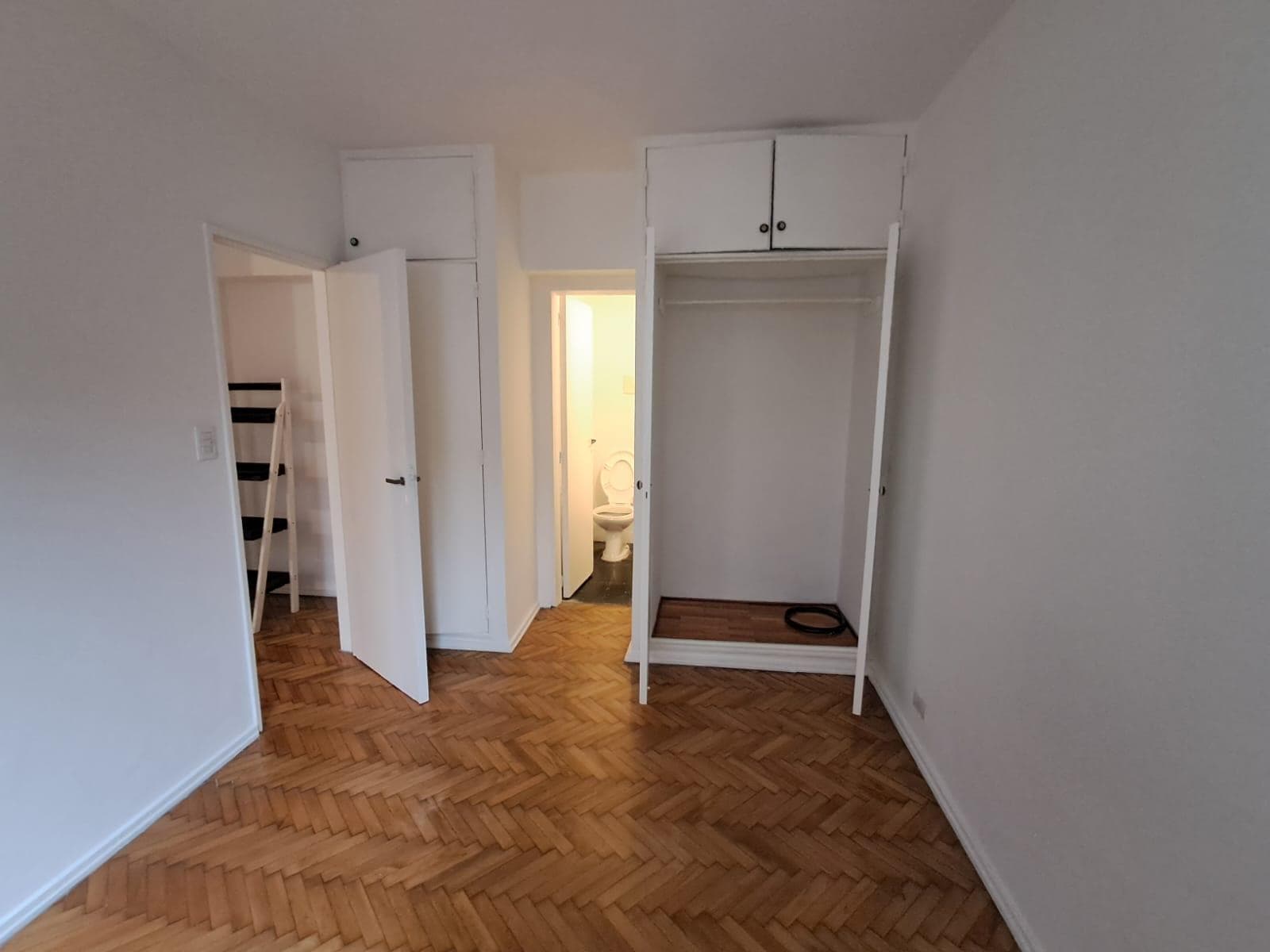 Dormitorio vacío con placares blancos y piso de madera en espiga.