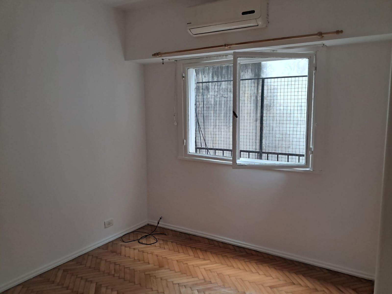 Dormitorio vacío con ventana enrejada y unidad de aire acondicionado.