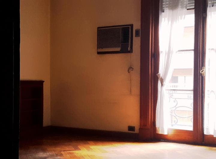 Living vacío con piso de madera y ventana con balcón francés.