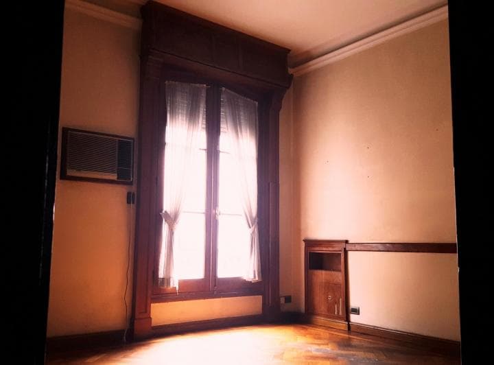Living vacío con grandes ventanas y mueble empotrado de madera.