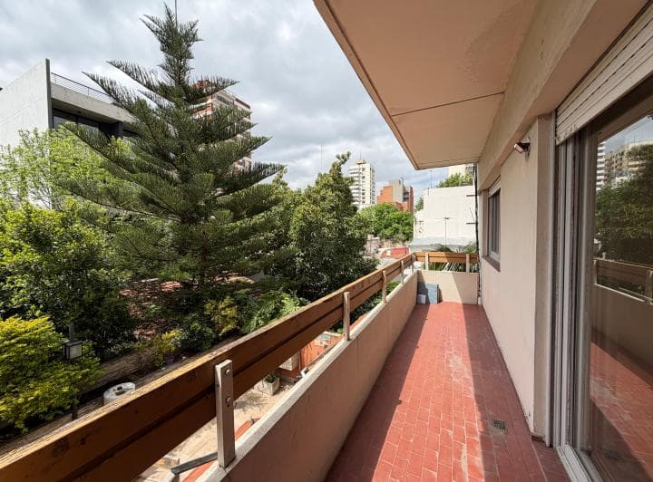 Balcón con baranda de madera y vista a árboles y edificios.