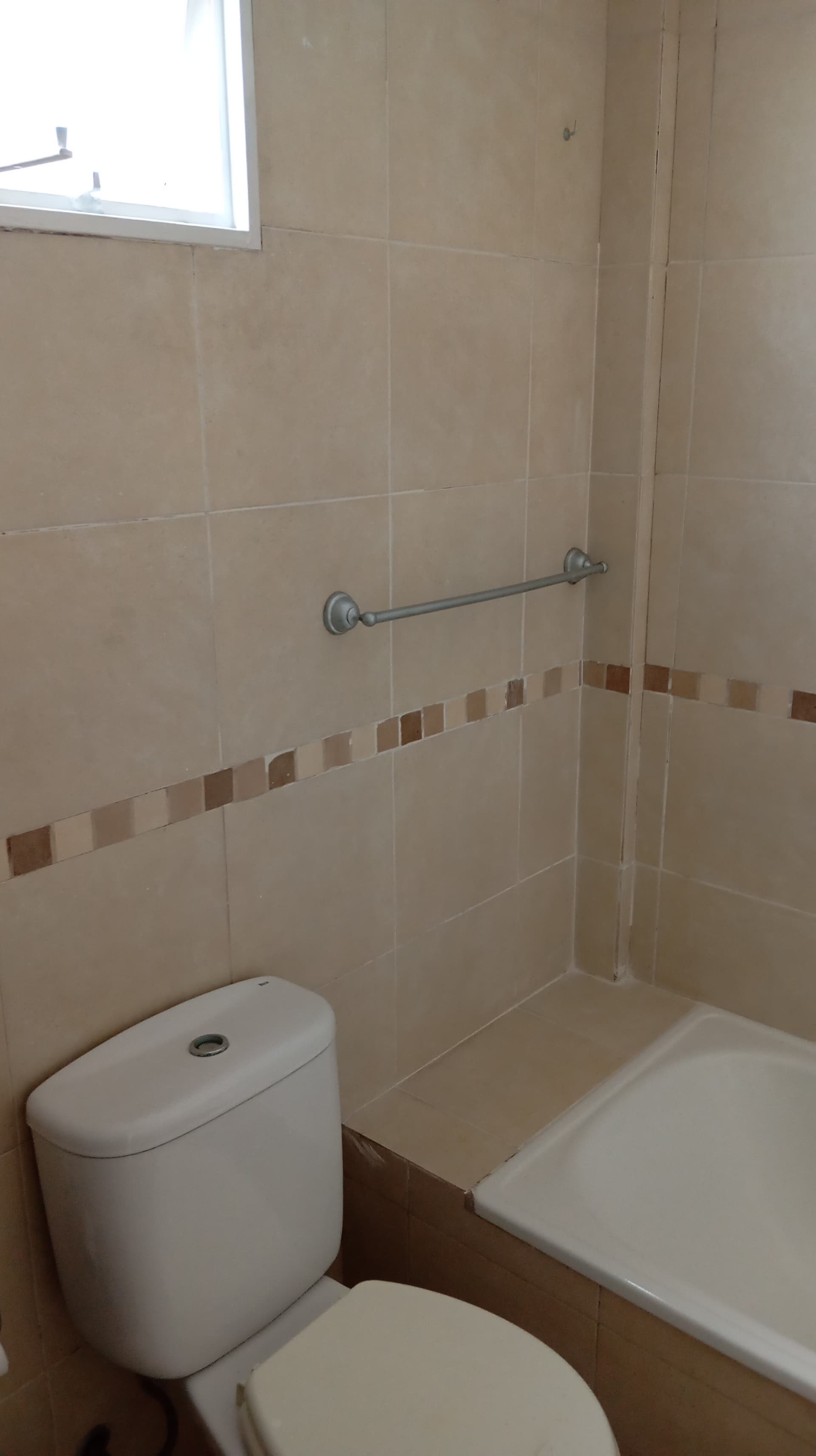 Baño con inodoro, bañera y azulejos beige en las paredes.