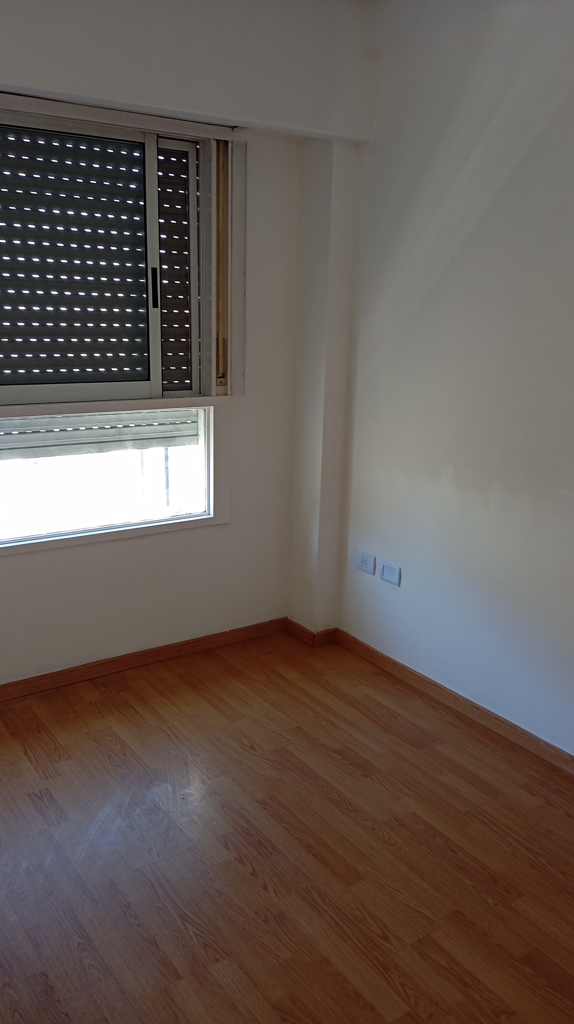 Dormitorio vacío con ventana y persiana, con piso de madera.